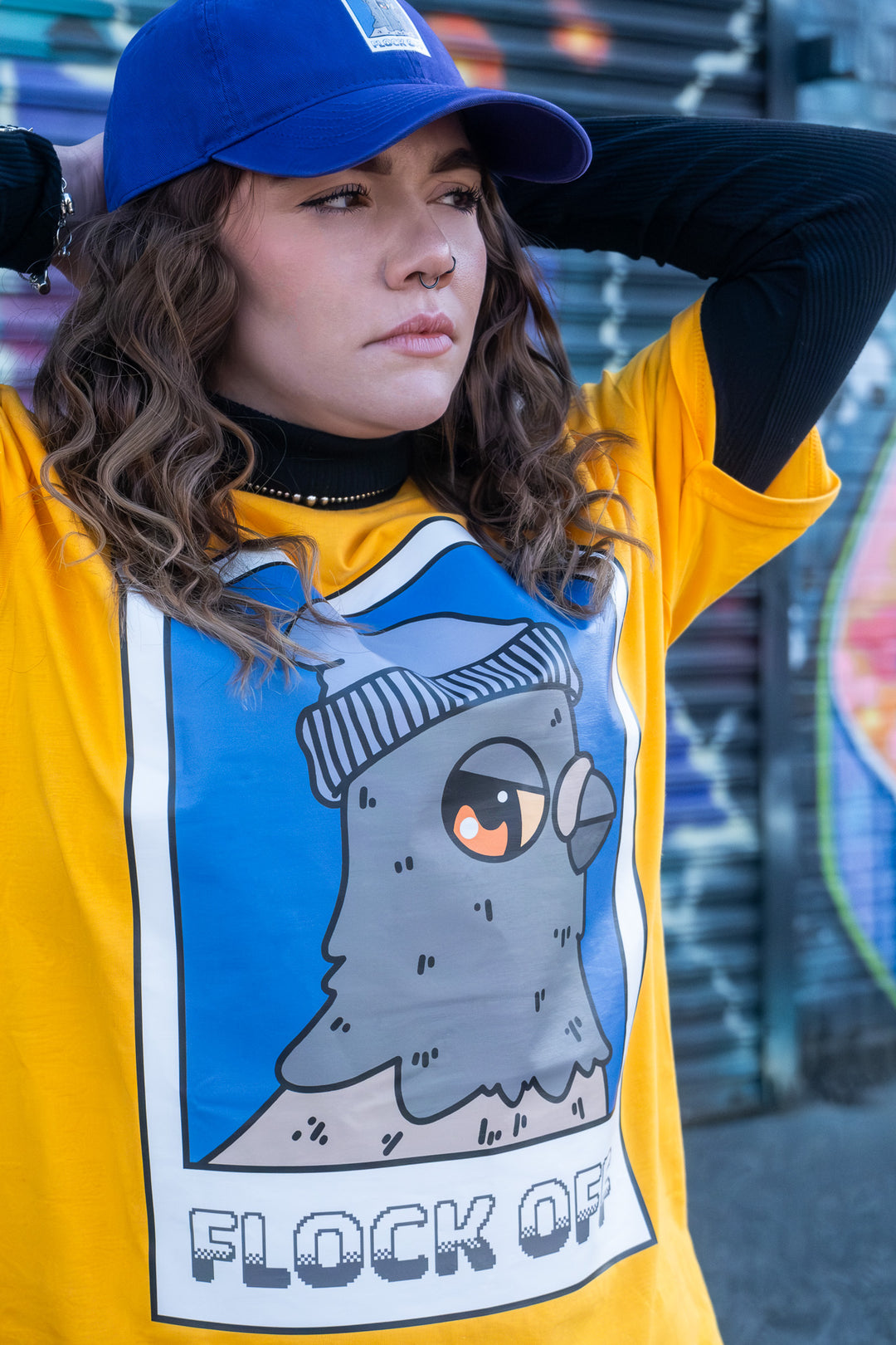 Close-up of a cartoon pigeon wearing a beanie, the focal print on a sunny yellow 'Flock Off' T-shirt, capturing the playful vibe.