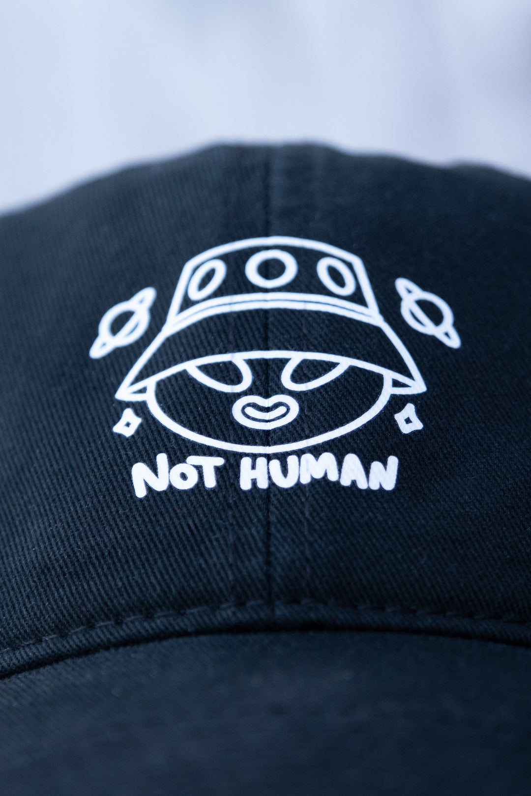 Close-up of a black low-profile 'dad' cap with a 'Not Human' alien design vinyl print on the front panel.